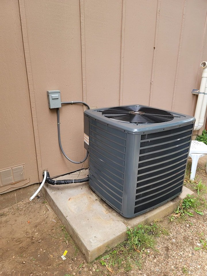 Goodman outdoor AC condenser installed on a concrete pad behind an Oklahoma City home — proper electrical disconnect and refrigerant line insulation visible